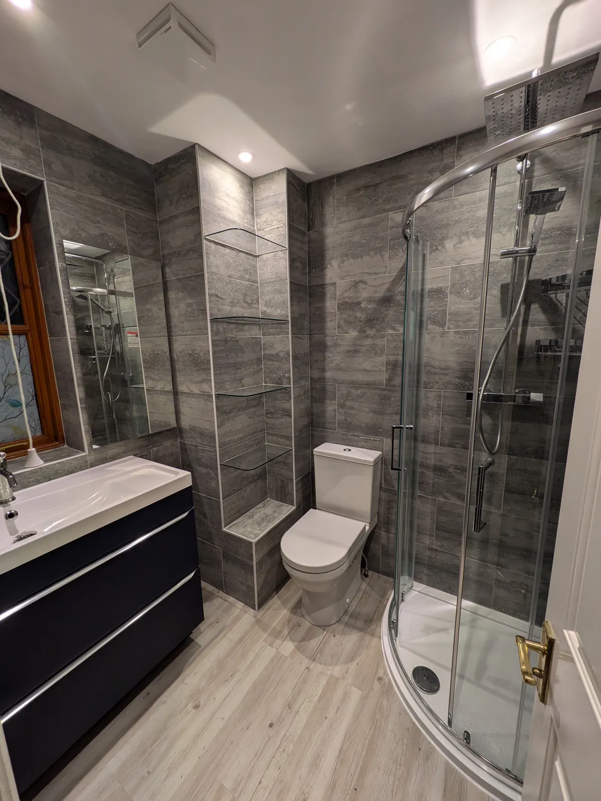 A finished bathroom with grey stone-effect tiling, a curved glass shower enclosure and a wall-hung vanity unit