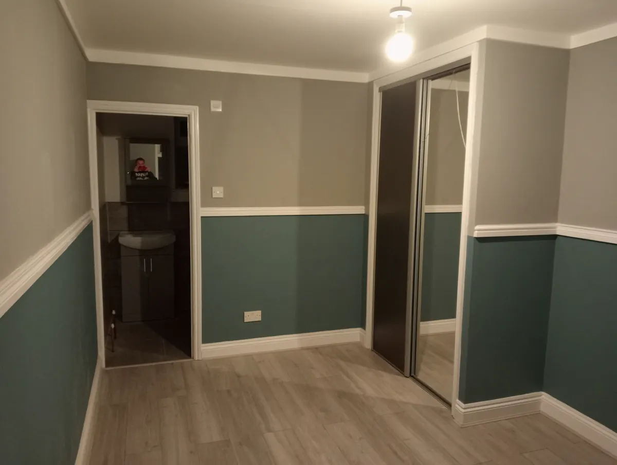 A finished bedroom hallway with two-tone grey and teal panelled walls, a wood-effect floor and a mirrored sliding wardrobe
